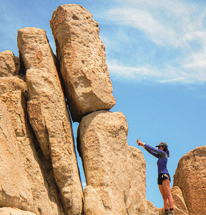 A person examining a large boulder with another boulder perched on top