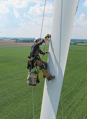 A person hanging from ropes high above the ground, working on a giant metal structure