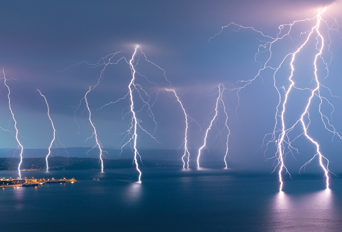 Enlargeable image of many lightning strikes at night across a city and the sea next to it