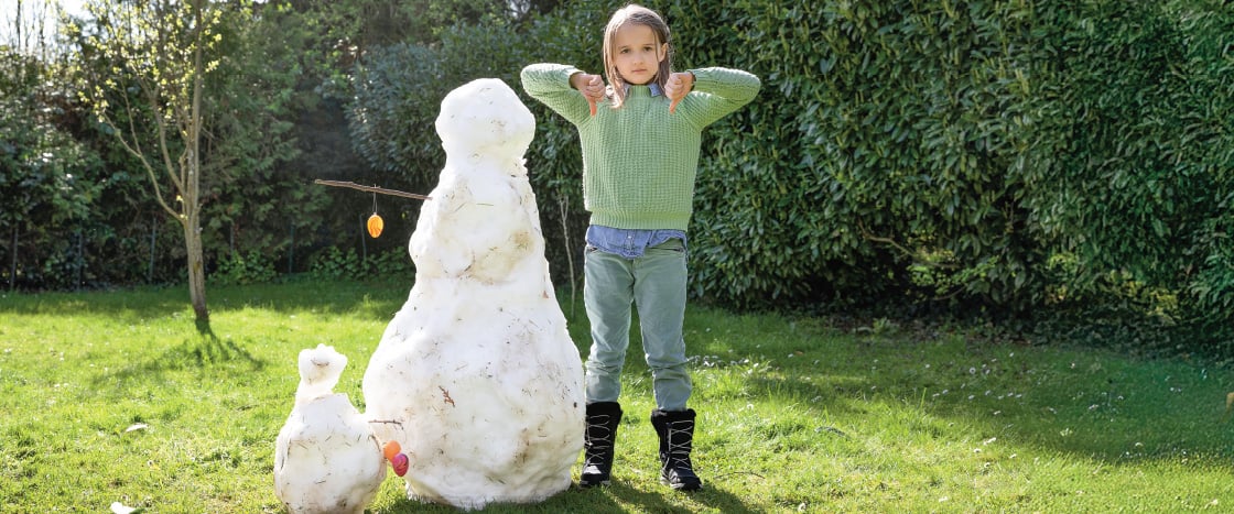 Image of student standing next to snowman on the grass during a sunny day