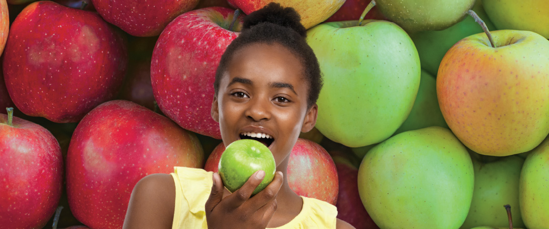 A girl bites into a green apple surrounded by red and green apples