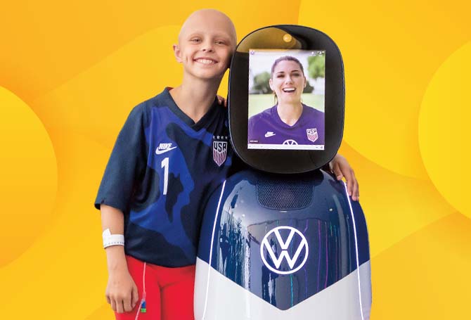 Kid standing next to a robot with a person using it to videochat