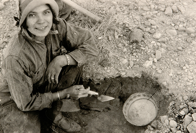 Black & white photo of an archaeologist finding a bowl in the ground